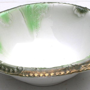 May include: A white ceramic bowl with a green and gold rim. The interior features green accents. The rim has a decorative, textured design with gold accents. The bowl is likely vintage and suitable for display or serving.