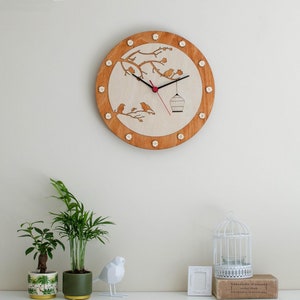 May include: A wooden clock with a bird and branch design. The clock face is white with black hands and a red center. The clock is surrounded by a brown wooden frame with white dots.