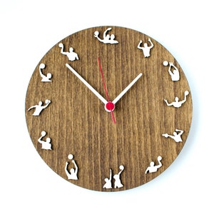 May include: A brown wooden clock with white silhouette images of people playing volleyball around the clock face. The clock hands are white with a red second hand.