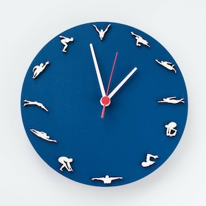 Könnte beinhalten: Eine blaue runde Uhr mit weißen Schwimmer-Silhouetten, die die Stunden markieren. Die Uhrzeiger sind weiß mit einem roten Sekundenzeiger.