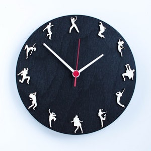 May include: A black clock with white silhouette dancers around the face. The clock hands are white with a red center.