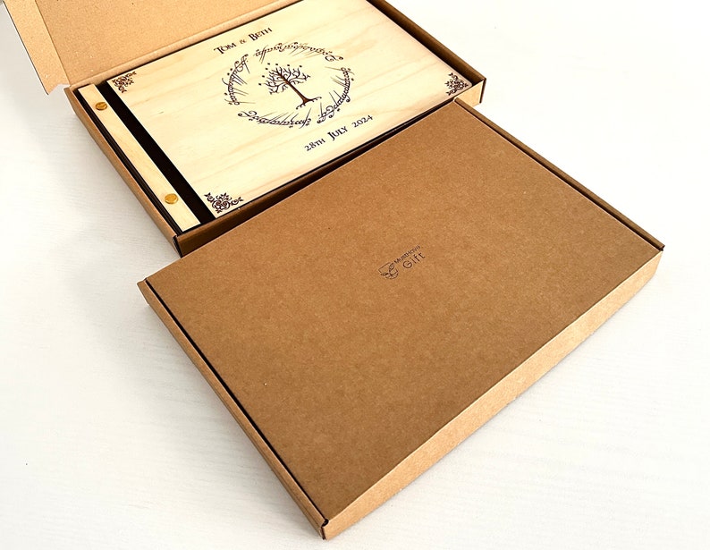 Pu&ograve; includere: Un libro degli ospiti in legno con una copertina nera e dettagli dorati. La copertina presenta un design inciso a laser di un albero con radici e il testo "Tom & Beth 28th July 2024". Il libro &egrave; confezionato in una scatola di cartone marrone.