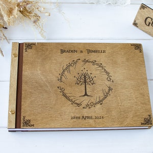Pu&ograve; includere: Un libro degli ospiti in legno con una spina dorsale in pelle marrone e accenti in metallo dorato. La copertina anteriore presenta un design inciso a laser dell'Albero Bianco di Gondor dal Signore degli Anelli, circondato dall'iscrizione "Un anello per domarli tutti, Un anello per trovarli, Un anello per portarli tutti e nell'oscurit&agrave; legarli." I testi "Braden & Tenielle" e "28th April 2023" sono anche incisi sulla copertina.