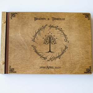 Pu&ograve; includere: Un libro degli ospiti in legno con una rilegatura in pelle marrone. La copertina anteriore presenta un design inciso a laser dell'Albero Bianco di Gondor dal Signore degli Anelli, circondato dall'iscrizione "Un anello per domarli tutti, Un anello per trovarli, Un anello per portarli tutti e nell'oscurit&agrave; legarli." I testi "Braden & Tenielle" e "28th April 2023" sono anche incisi sulla copertina.