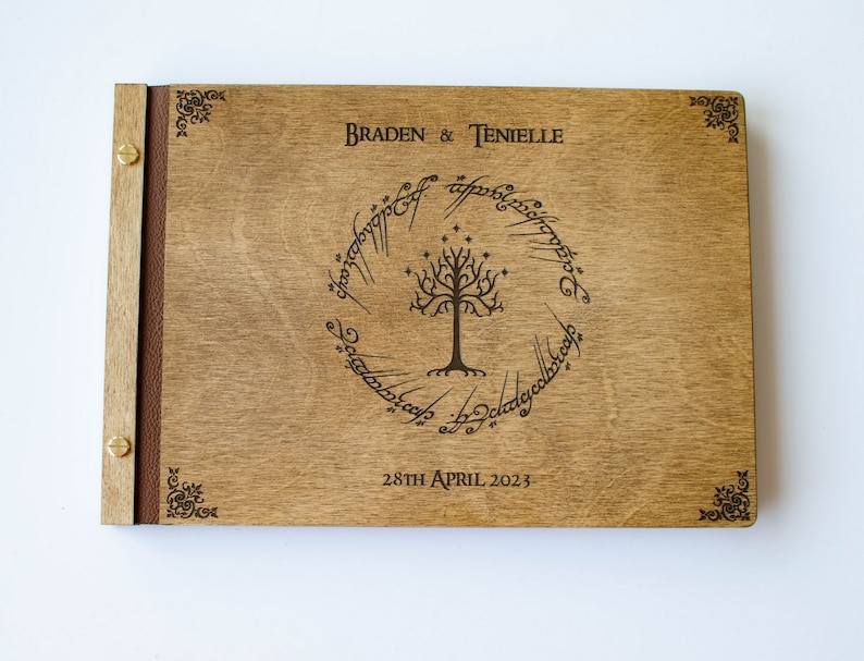 Pu&ograve; includere: Un libro degli ospiti in legno con una rilegatura in pelle marrone. La copertina anteriore presenta un design inciso a laser dell'Albero Bianco di Gondor dal Signore degli Anelli, circondato dall'iscrizione "Un anello per domarli tutti, Un anello per trovarli, Un anello per portarli tutti e nell'oscurit&agrave; legarli." I testi "Braden & Tenielle" e "28th April 2023" sono anche incisi sulla copertina.