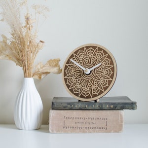 May include: A wooden clock with a mandala design and white hands. The clock is sitting on top of a stack of books.