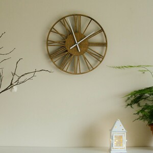May include: A wooden clock with Roman numerals on a white wall, a vase with dried branches, and a white lantern on a shelf with a potted plant.