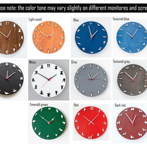 Puede incluir: Un conjunto de 12 relojes de pared redondos con diferentes fondos de colores y figuras blancas de personas haciendo ejercicio alrededor de la esfera del reloj. Las esferas de los relojes son todas del mismo dise&ntilde;o con manecillas negras y un punto central rojo. Los colores de los relojes son: madera oscura, madera clara, azul, azul texturizado, negro, blanco, gris, gris texturizado, verde esmeralda, rojo, rojo oscuro.