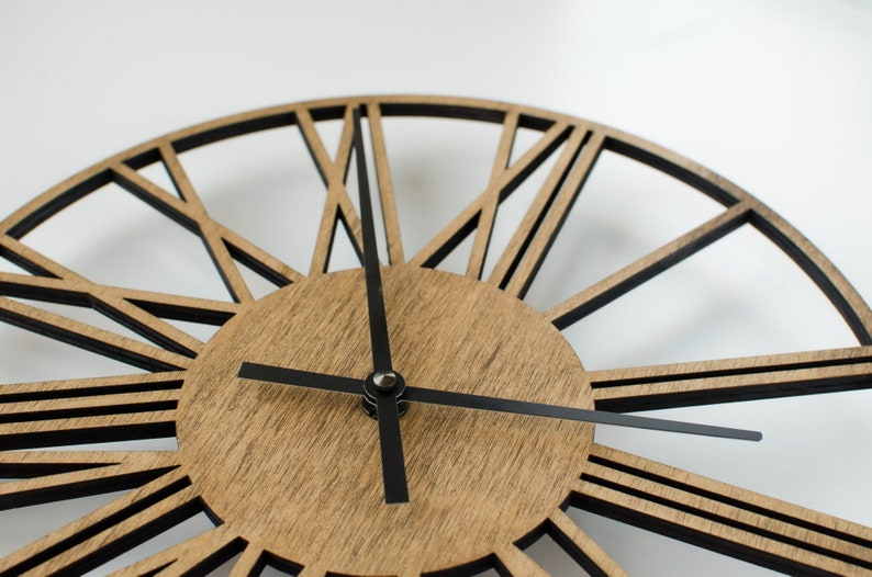 A brown wooden clock with black Roman numeral hour markers and black hands. The clock has a geometric design with black lines radiating from the center.