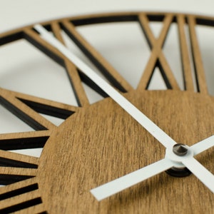 May include: A close-up of a wooden clock face with white hands. The clock face has a unique design with black lines radiating out from the center.