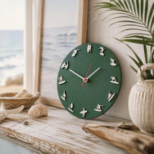 May include: A round wall clock with a dark green face featuring twelve white silhouettes of surfers in various poses as hour markers. The clock has two white hour and minute hands and a thin red second hand centered on the circular green dial.