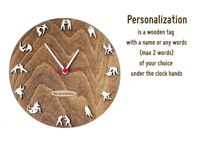 Puede incluir: Un reloj de madera marr&oacute;n con figuras blancas de personas en una pose de lucha alrededor de la esfera del reloj. Las manecillas del reloj apuntan a las 12:30. El texto "Your personalization" est&aacute; impreso en una peque&ntilde;a etiqueta de madera debajo de las manecillas del reloj. El texto "Personalization is a wooden tag with a name or any words (max 2 words) of your choice under the clock hands" est&aacute; impreso en texto marr&oacute;n sobre un fondo blanco.