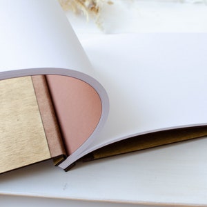 Pu&ograve; includere: Un diario rilegato in pelle marrone con una copertina in legno e pagine bianche vuote. Il diario &egrave; aperto per rivelare le pagine vuote.