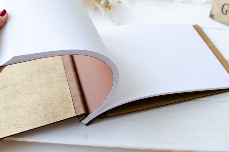 Pu&ograve; includere: Un diario rilegato in pelle marrone con una copertina in legno e pagine bianche vuote. Il diario &egrave; aperto per rivelare le pagine vuote.