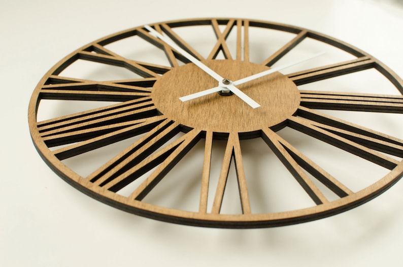 May include: A large, round, wooden wall clock with Roman numeral markings and white hands. The clock face is made of wood with a light brown finish. The clock has a decorative, open-work design.