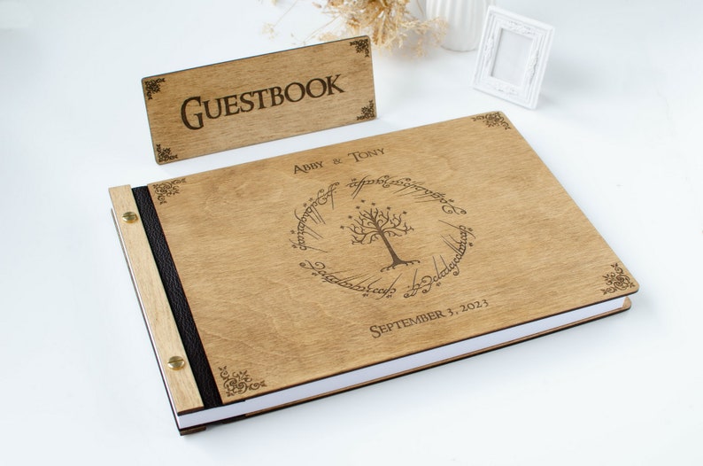 Pu&ograve; includere: Un libro degli ospiti in legno con una rilegatura in pelle nera e un design inciso a laser dell'Albero Bianco di Gondor dal Signore degli Anelli. La copertina include anche i nomi "Abby & Tony" e la data "3 settembre 2023".