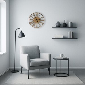 May include: A gray armchair with black legs sits in a living room with a black side table, a floor lamp, and a large round clock with Roman numerals on the wall.