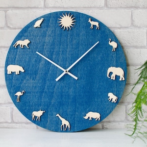 May include: A blue wooden clock with white animal silhouettes, including a lion, elephant, rhino, and giraffe. The clock has white hands and a white sun in the center.