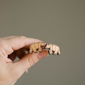 Puede incluir: Dos figuritas de oso de madera que se miran. Los osos están hechos de madera marrón claro y tienen un diseño geométrico.