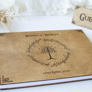 Pu&ograve; includere: Un libro degli ospiti in legno con una spina dorsale in pelle marrone. La copertina presenta un design inciso dell'Albero Bianco di Gondor dal Signore degli Anelli, circondato dall'iscrizione "Un solo anello per governarli tutti." Il libro &egrave; intitolato "Braden & Tenielle" e la data "28 aprile 2023" &egrave; stampata sotto il design.