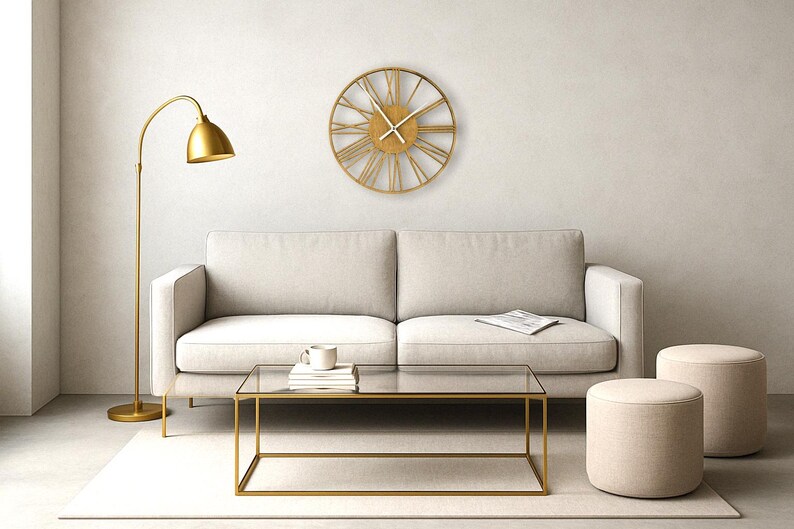May include: A gold-toned metal clock with Roman numeral markings hangs on a white wall above a white sofa. A gold floor lamp, a glass coffee table, and two beige ottomans are in the room.