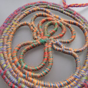 May include: A circular wall hanging made of woven yarn in shades of orange, green, blue, and purple. The yarn is woven into a complex pattern that resembles a flower or a star.