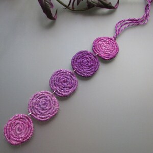 Peut inclure: Une suspension murale en fil de laine ombrée de couleur violette et rose avec cinq pièces tissées circulaires reliées par une fine ficelle.