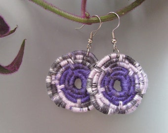 May include: A pair of purple and white circular earrings with a silver hook. The earrings are made of woven yarn.