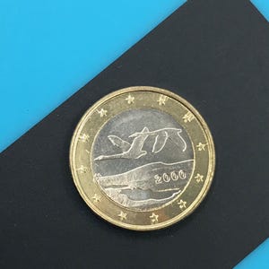 Può includere: Una moneta color oro con un centro argentato raffigurante tre uccelli in volo sopra un paesaggio. L'anno 2000 è visibile. La moneta è posta su uno sfondo nero e uno sfondo blu.