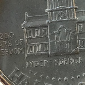 May include: A close-up of a silver half dollar coin. The coin features an image of Independence Hall and the text "200 YEARS OF FREEDOM" and "INDEPENDENCE". The word "HALF DOLLAR" is also visible.