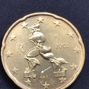 Puede incluir: Una moneda de 20 céntimos de euro italiana de color dorado de 2002 con la escultura Formas únicas de continuidad en el espacio de Umberto Boccioni. La moneda muestra las letras R, IR y M.A.C. con un pequeño círculo que amplía un detalle.