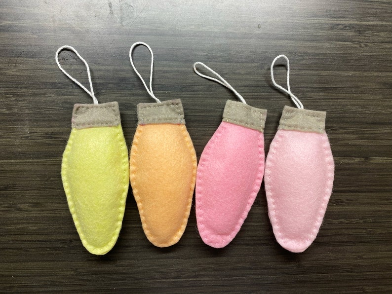 May include: Four felt lightbulb ornaments in yellow, orange, pink, and light pink with white string loops.