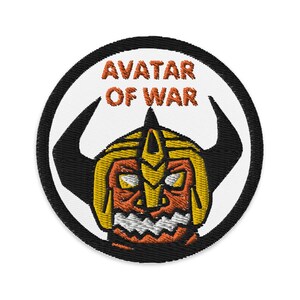 May include: A round, white patch with a black border. The patch features a yellow and orange cartoon monster with horns and a helmet. The text "AVATAR OF WAR" is written in orange above the monster.