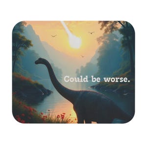 Puede incluir: Un posavasos cuadrado con esquinas redondeadas, que representa un dinosaurio en un lago con una puesta de sol y el texto "Could be worse". La imagen incluye montañas, árboles y un meteorito. Diseño humorístico.