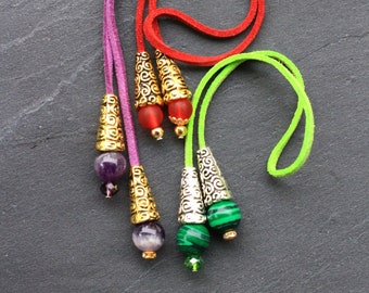 May include: Four colorful leather cord bookmarks with decorative metal and gemstone tips. The tips include a red, purple, amethyst, and green stone.