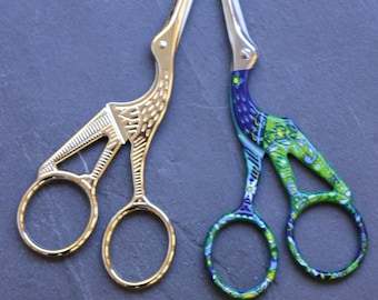 May include: Two pairs of decorative scissors with bird-shaped handles. One pair is silver with a simple design, and the other pair is green and blue with a floral pattern.