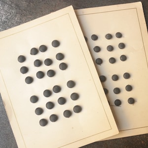 May include: Two cards with black buttons arranged in rows. The buttons are round and have a textured surface.