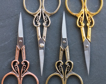 May include: Three pairs of decorative scissors with ornate handles. The scissors are silver, gold, and copper in color.