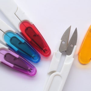 May include: Four pairs of small white handled scissors with coloured plastic blades. The blades are red, blue, purple, and a pair of silver blades with a white handle.