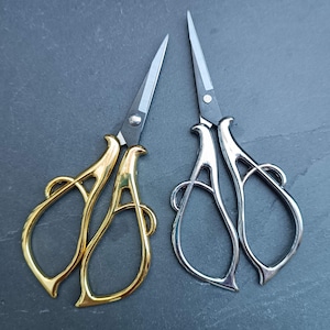 Könnte beinhalten: Zwei Paare dekorativer Scheren mit verzierten Griffen. Ein Paar ist golden und das andere ist silbern.