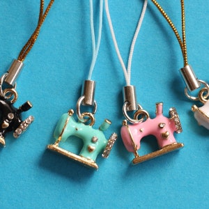 May include: Four miniature sewing machine charms attached to thin metallic and nylon cords. The charms are finished in black, mint green, pink, and white enamel with gold-tone metal accents and small clear crystals embedded on the side wheels.