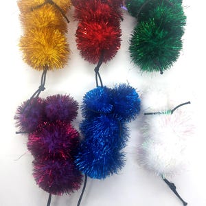 May include: Six colorful fluffy cat toys with long strings. The toys are in the colors gold, red, green, purple, blue, and white.