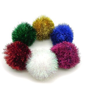 May include: Six colorful fluffy pom poms in red, green, blue, white, gold, and pink. The pom poms are arranged in a circle on a white background.