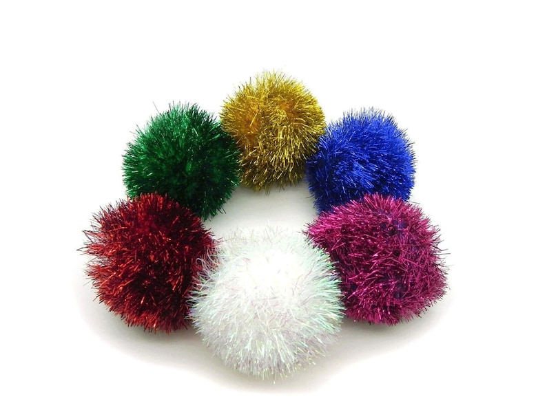 May include: Six colorful fluffy pom poms in red, green, blue, white, gold, and pink. The pom poms are arranged in a circle on a white background.