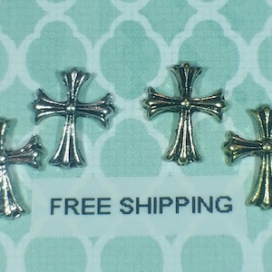May include: Four silver and gold cross charms. The crosses are ornate and have a raised center. The charms are on a light green background with a white pattern.