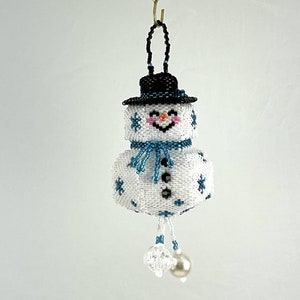 Peut inclure: Une décoration de Noël en forme de bonhomme de neige en perles blanches avec un chapeau noir, une écharpe bleue et des flocons de neige blancs. Le bonhomme de neige a un nez rond noir et une bouche souriante rose.