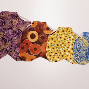 May include: Four fabric face masks with different patterns. The masks are purple with gold flecks, brown with orange circles, yellow with sunflowers, and blue with paisley patterns.