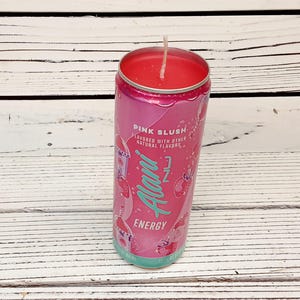 May include: A pink candle in a repurposed Alani Nu Energy drink can. The can features the words "Pink Slush" and "Energy" in a stylized font. The candle wax is a vibrant pink, and a white wick is centered.