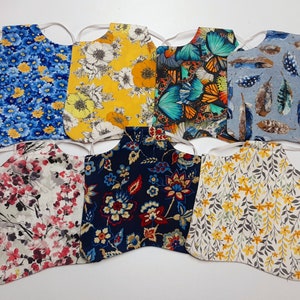 Könnte beinhalten: Acht Stoffmasken mit verschiedenen Blumenmustern. Die Masken sind aus Baumwolle und haben verstellbare Ohrschlaufen. Die Muster umfassen blaue Blumen, gelbe Blumen, Schmetterlinge, Federn, rosa Blumen, rote Blumen, gelbe Blumen mit grauen Blättern und graue Blätter mit gelben Blumen.