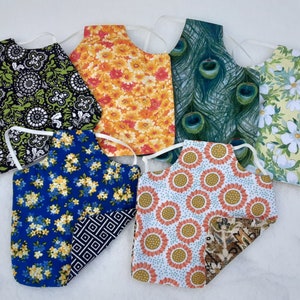 May include: Six different fabric aprons with various floral and patterned designs. The aprons are made of cotton and have adjustable straps.